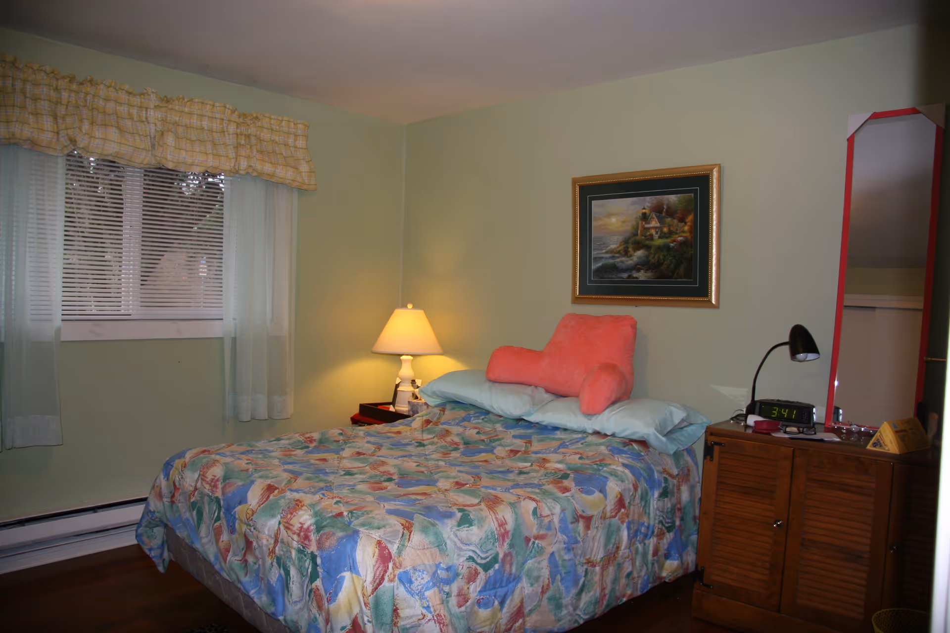 Simple bedroom with a bed, lamp, dresser, window, artwork, and green walls.