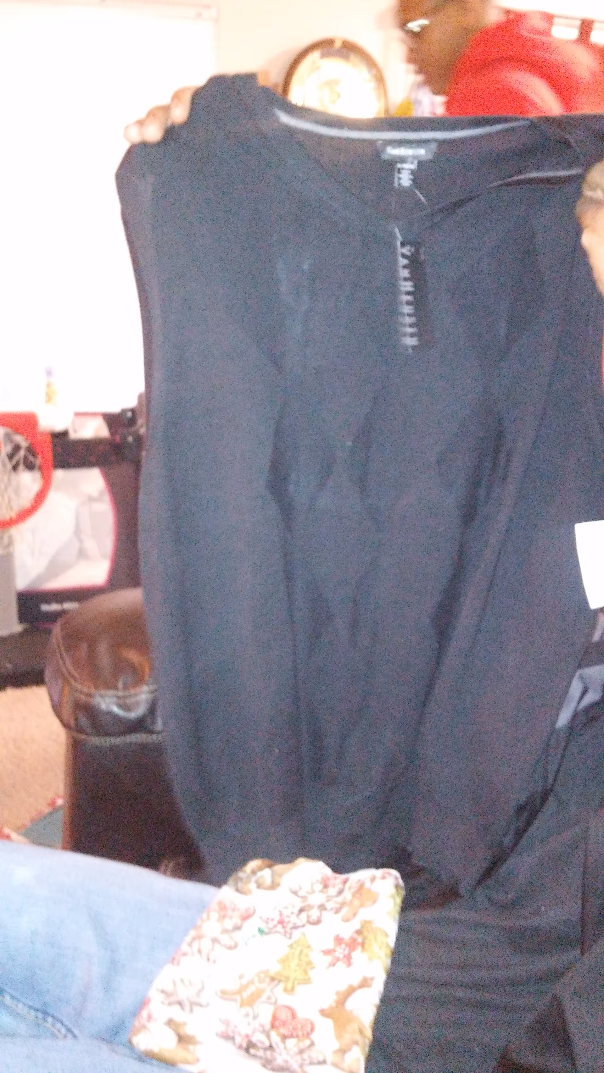 Person holds up a large black garment in a cluttered living room.