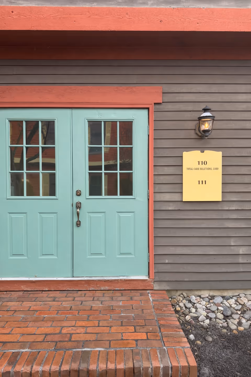 Teal double doors set in brown siding with a yellow Total Care Solutions plaque.