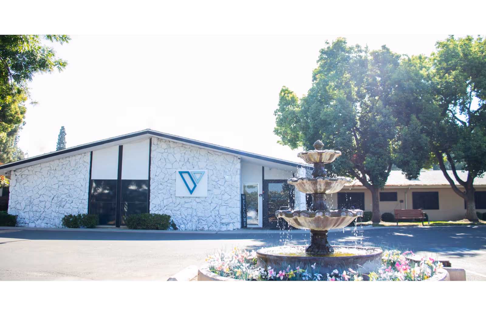 Front exterior of Redwood Springs Healthcare Center with a tiered fountain and trees.