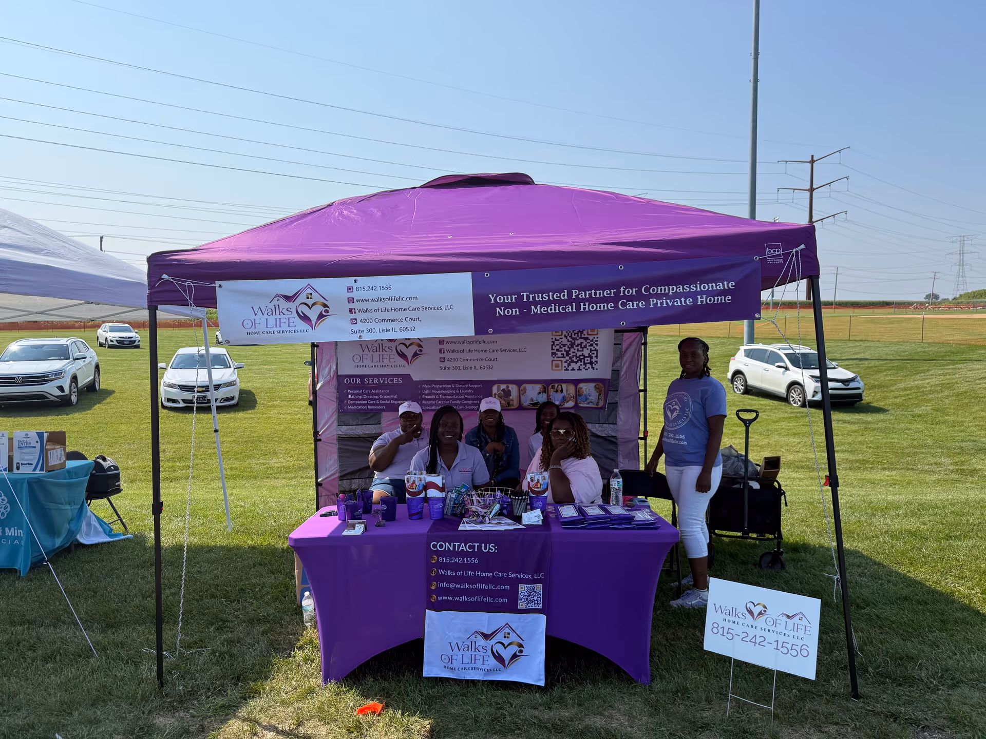 Purple tent booth with staff at a table promoting Walks of Life Home Care Services outdoors.