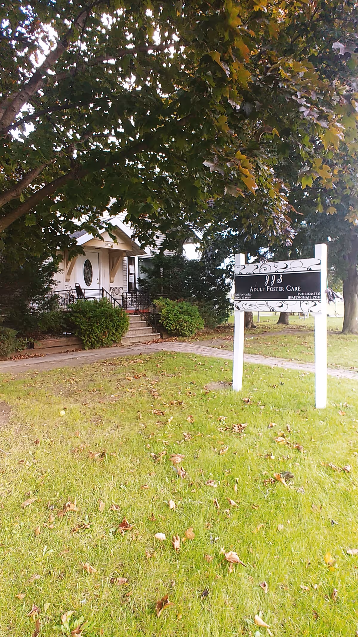 Exterior of JJS Adult Foster Care Home with sign and entrance under trees.