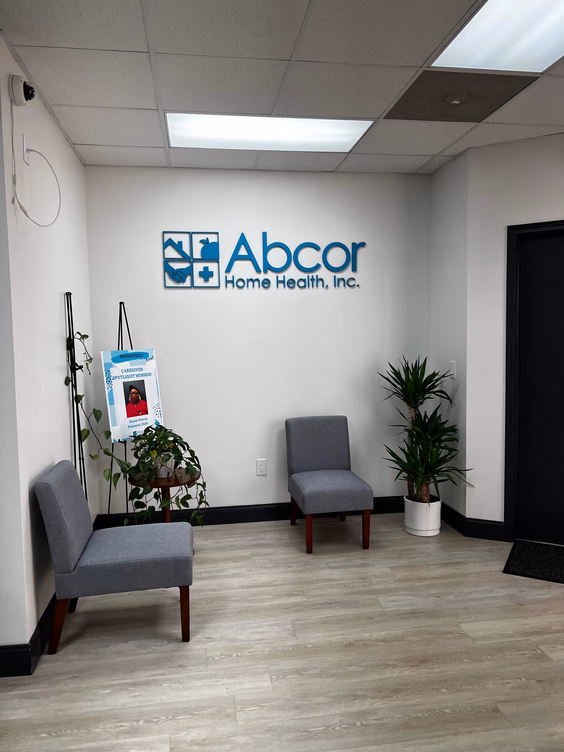 Lobby seating area with Abcor Home Health logo on wall, two gray chairs, and plants.