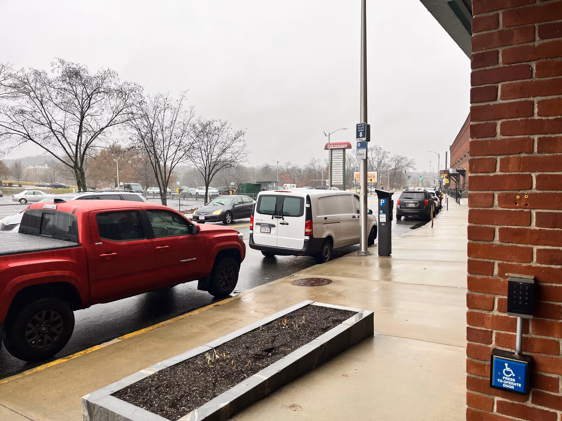 Street view outside a brick building with parked cars along a wet sidewalk.
