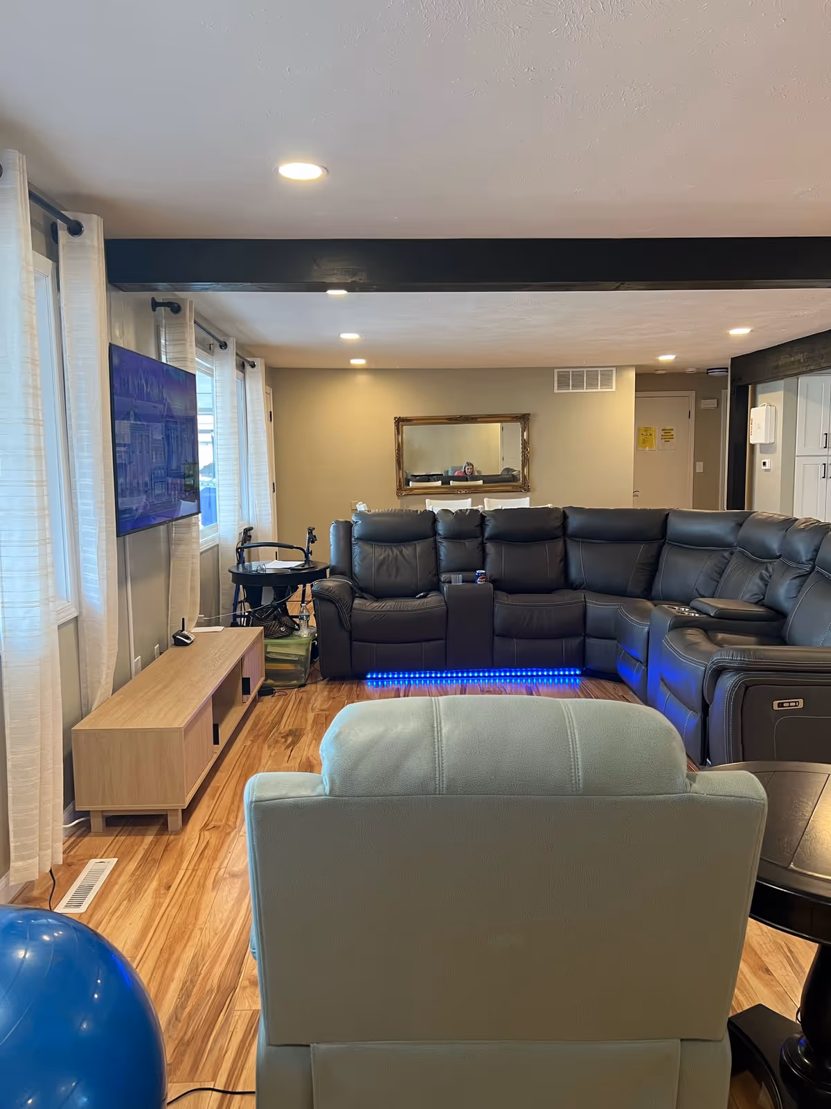 Cozy living room with a black sectional, blue lighting, and a wall-mounted TV.