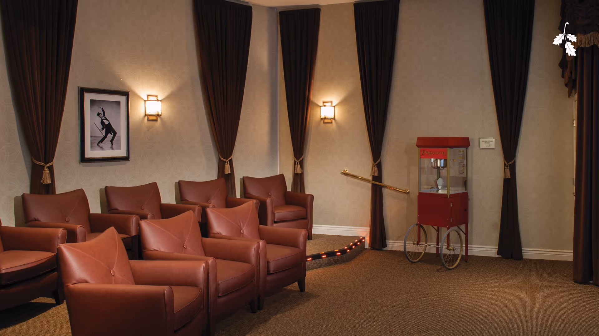 Rows of red leather chairs in a theater-style lounge with dark curtains and a popcorn cart.