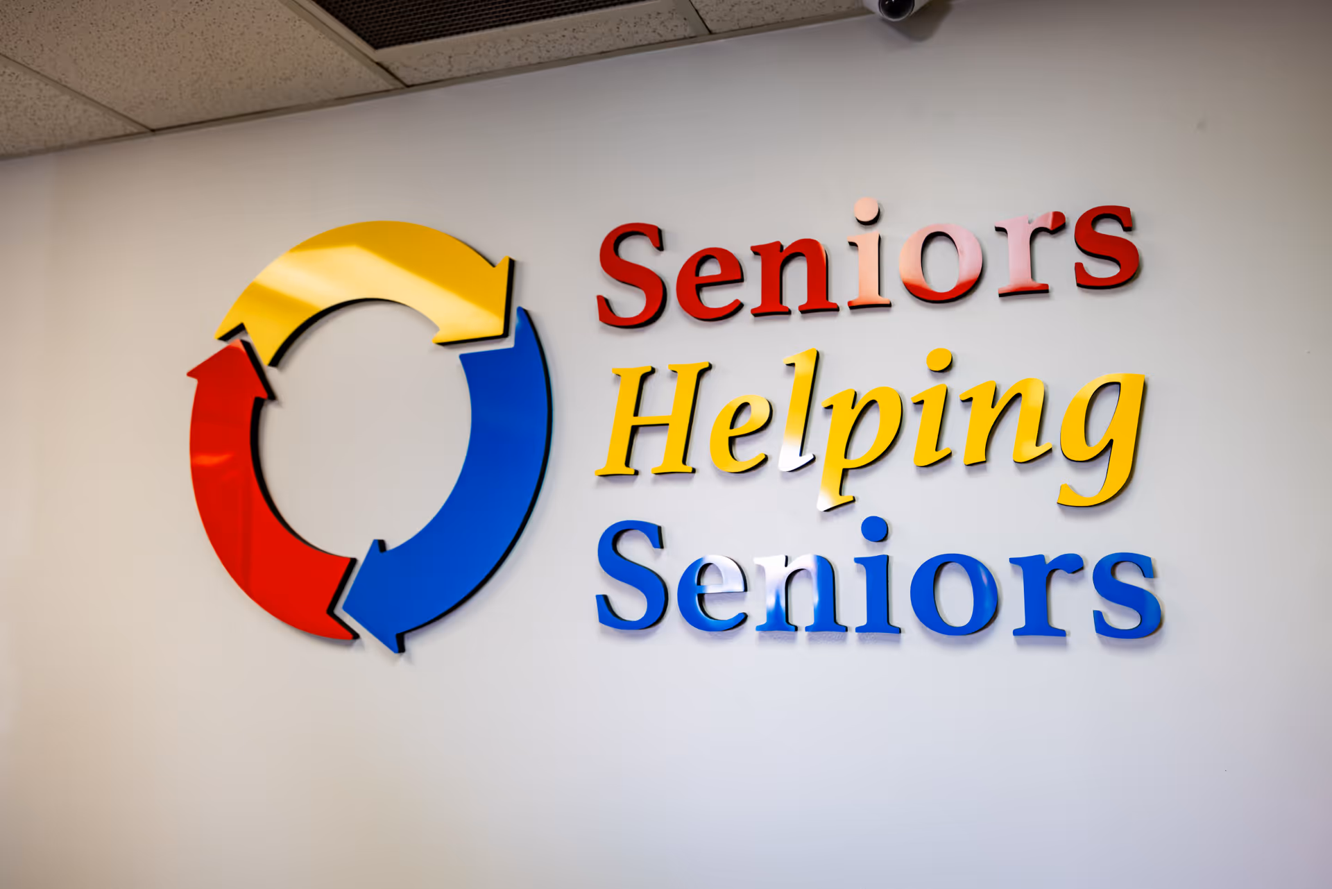 Interior wall sign reading Seniors Helping Seniors with a multicolor circular logo.