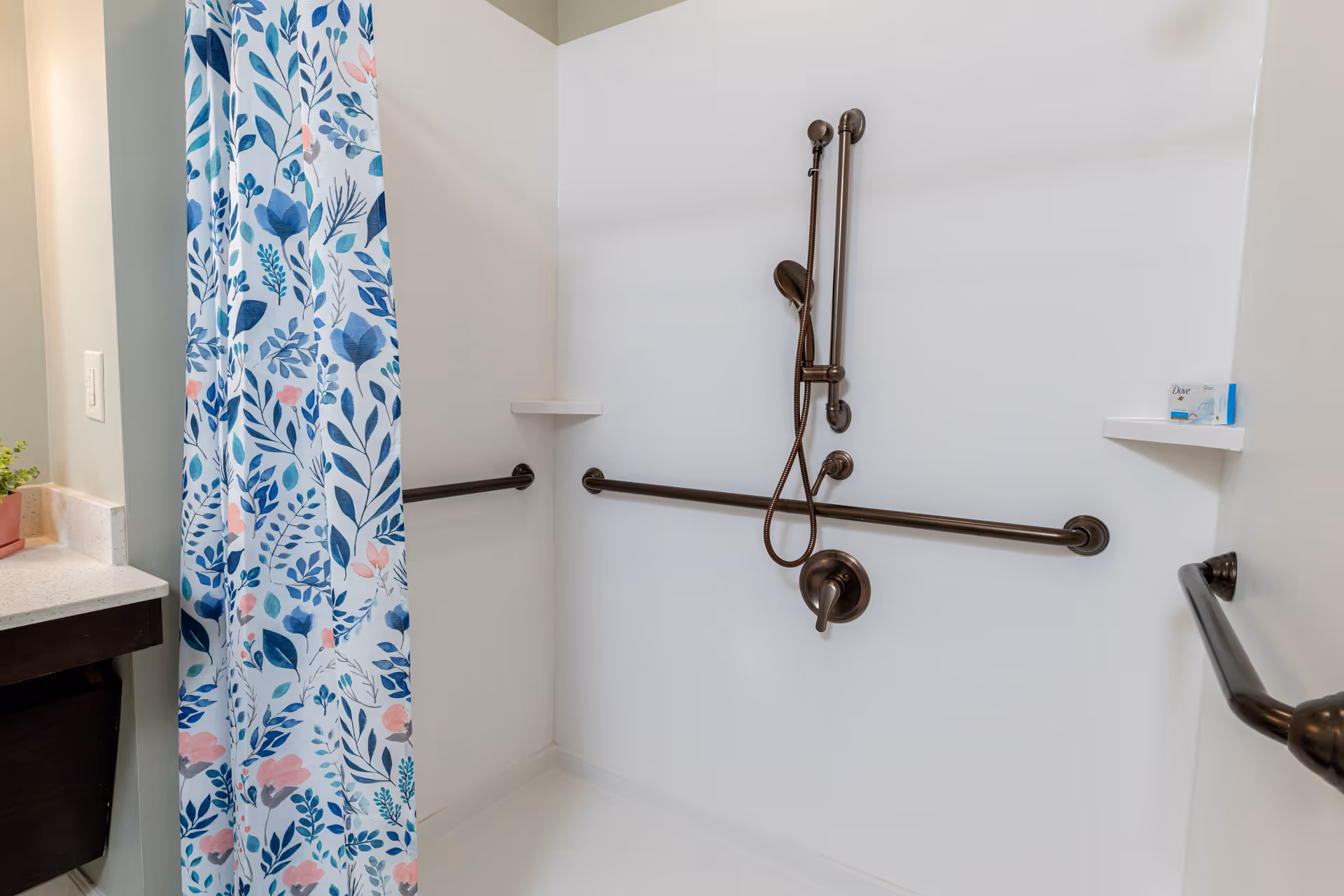 Accessible bathroom with brown grab bars, a handheld shower, and floral curtain.