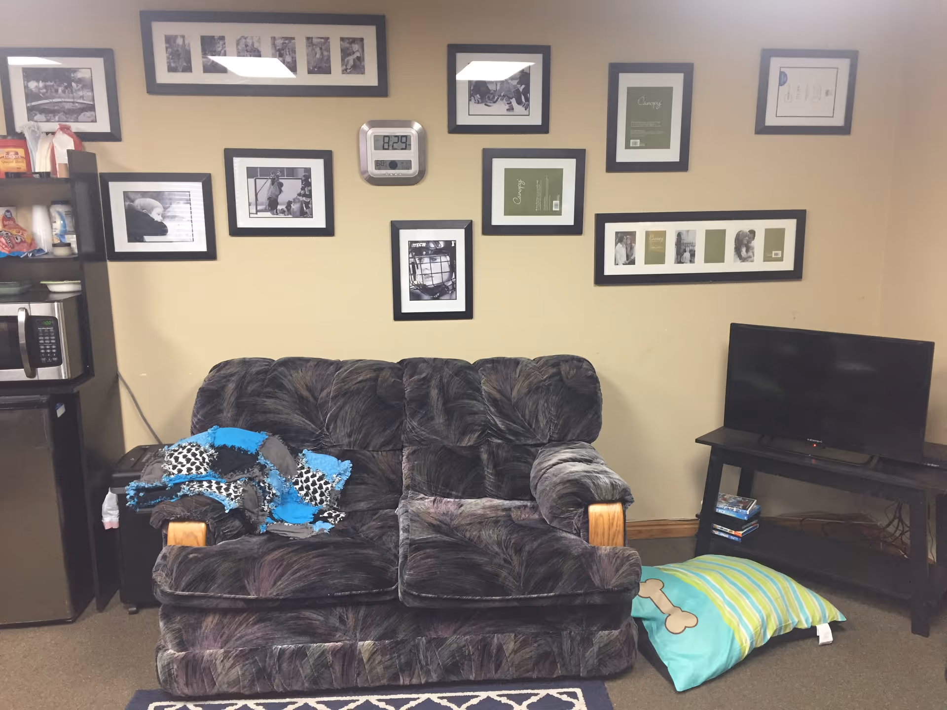 A cozy living room in a senior facility with a couch, framed photos, and a TV.