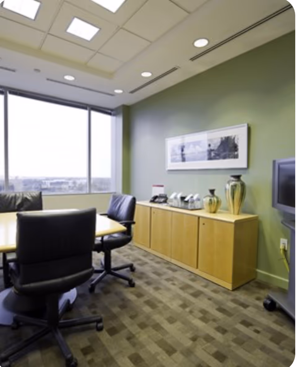Interior meeting room with green wall, wooden cabinet, conference table, and black office chairs.