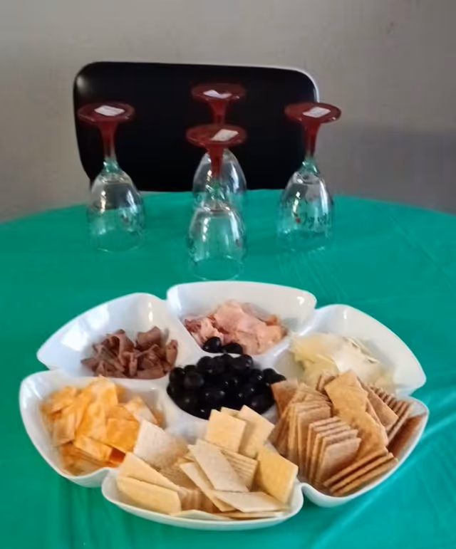 Platter with crackers, cheese, olives on a green table with upside-down wine glasses.