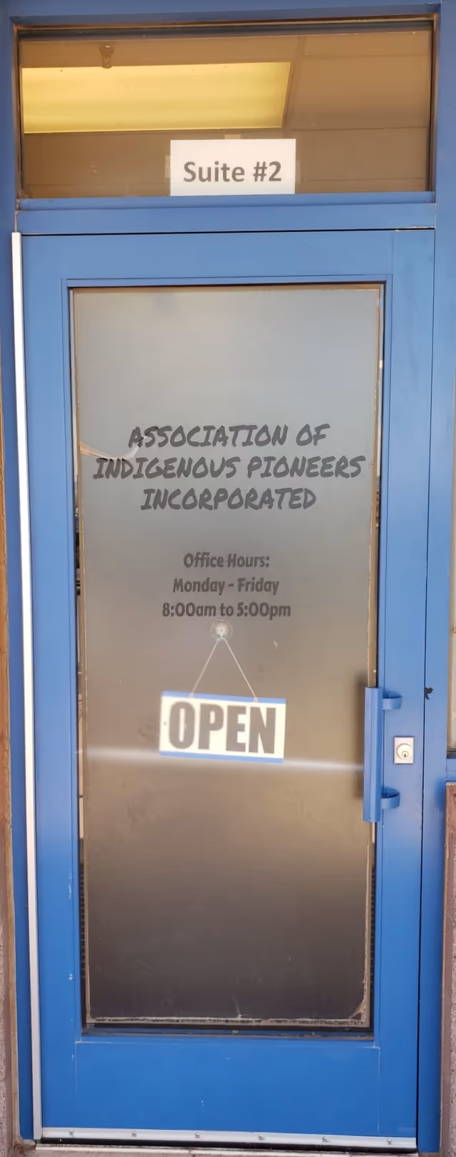 Blue building entrance door with OPEN sign and text for Association of Indigenous Pioneers, Incorporated.