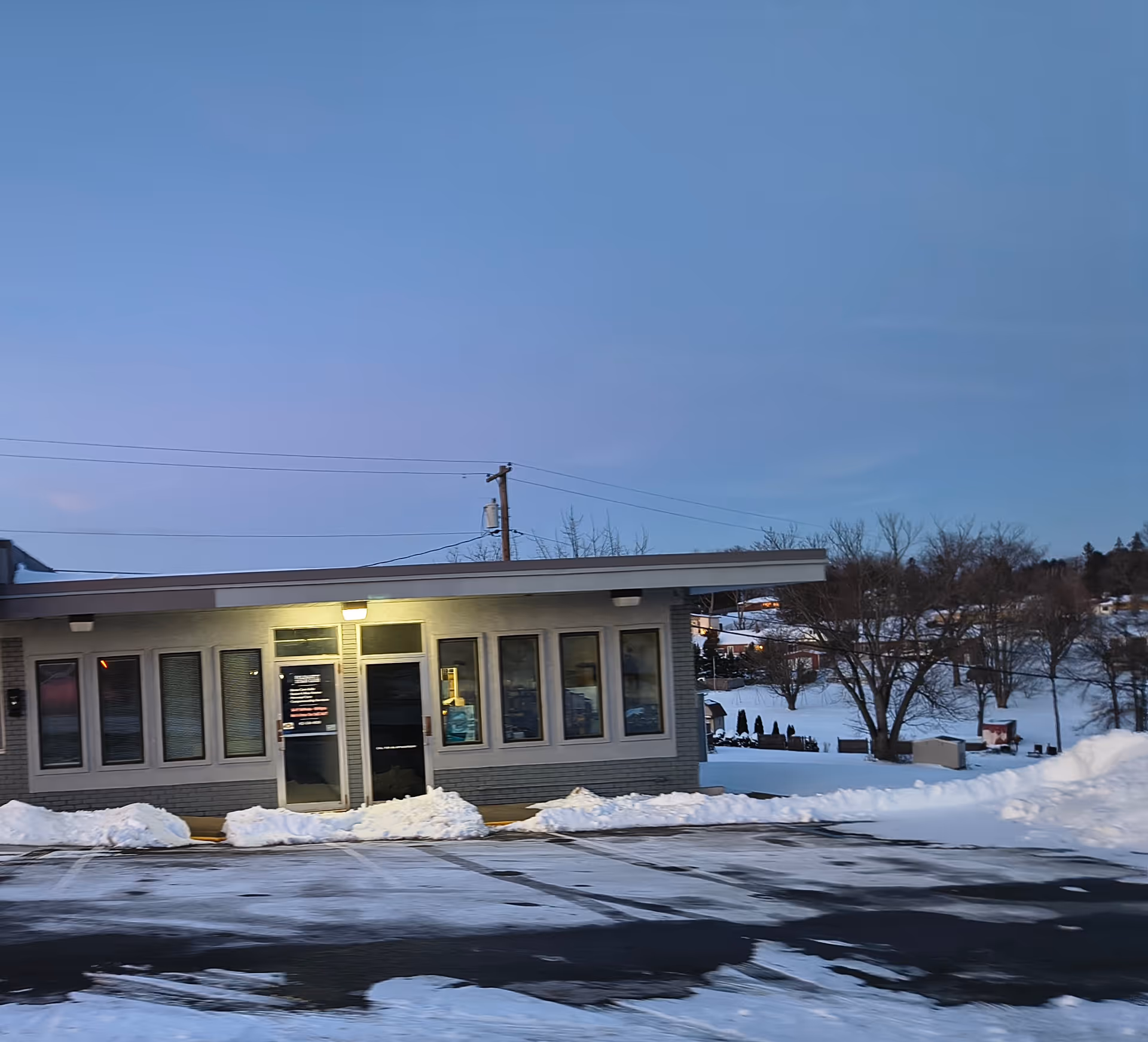 Front view of a single-story building with snow-covered ground and a parking lot.