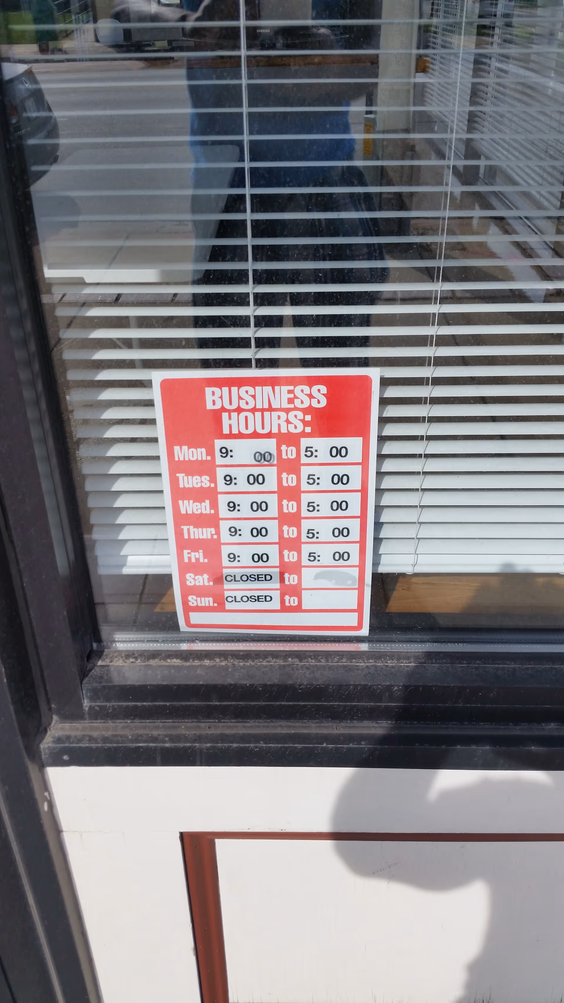 Glass storefront door with horizontal blinds and a red business hours sign.