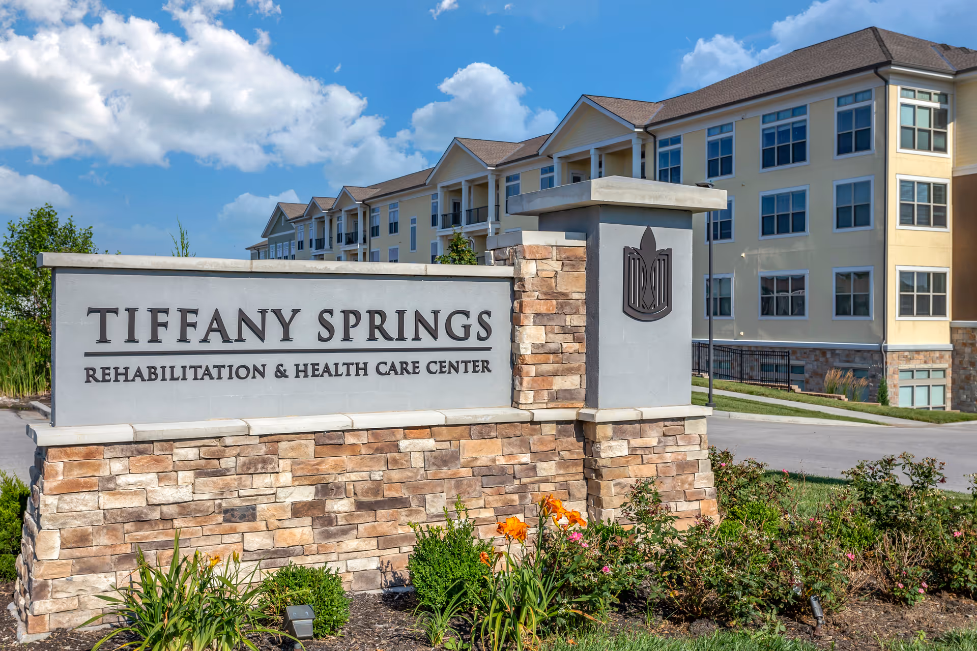 Front view of Tiffany Springs Rehabilitation & Health Care Center sign with building behind.