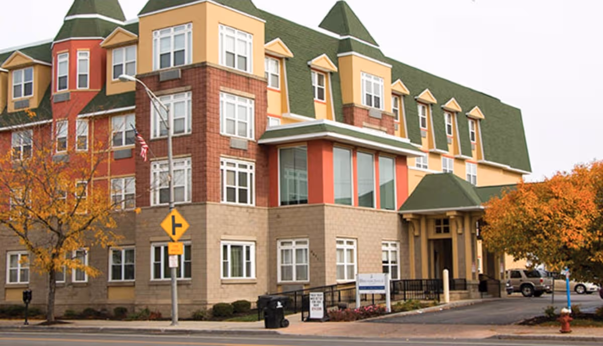 Colorful, multi-story senior living facility with a covered entrance and autumn trees outside.