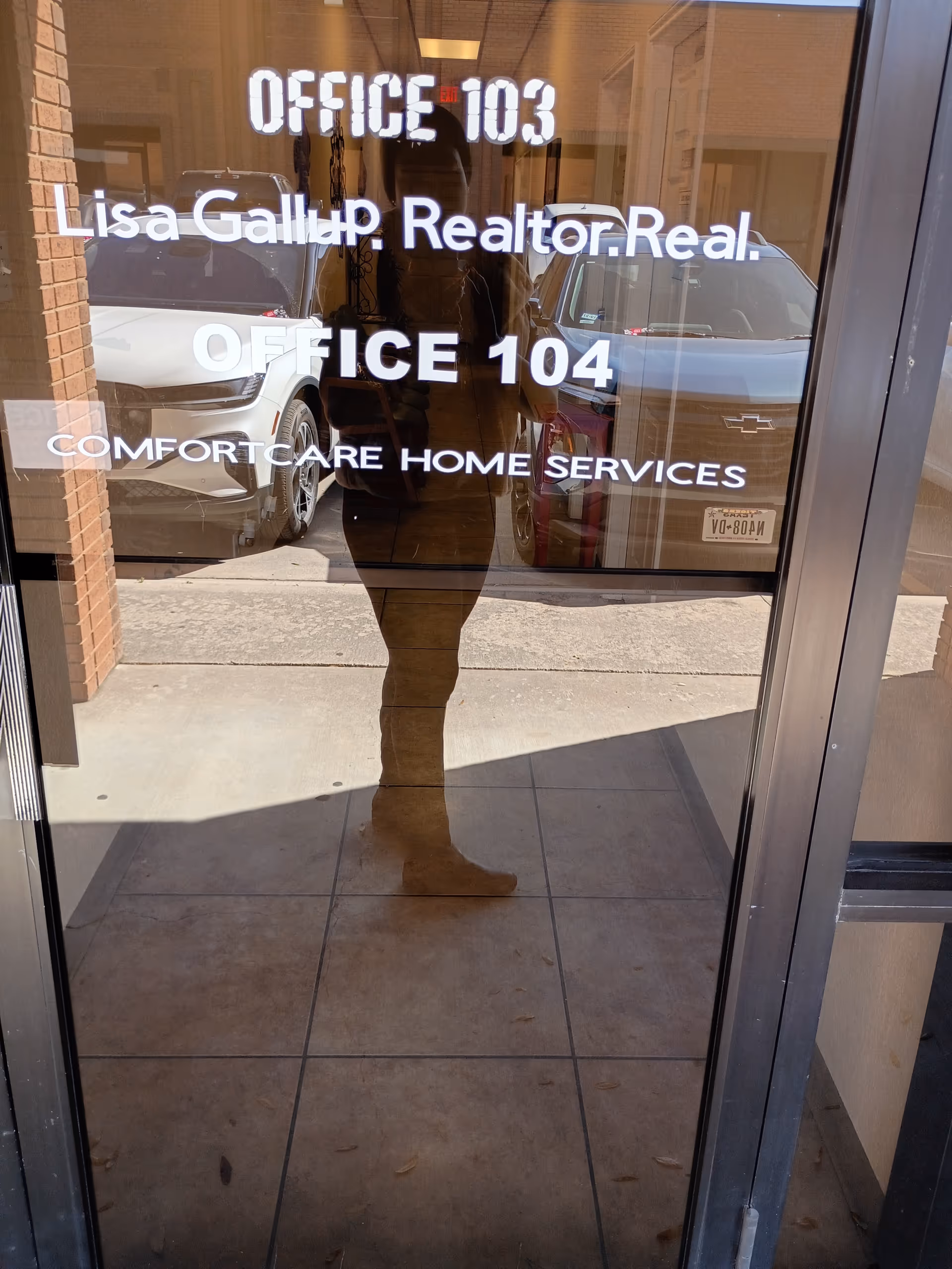 Glass entrance door shows OFFICE 103/104 and ComfortCare Home Services branding; photographer's reflection
