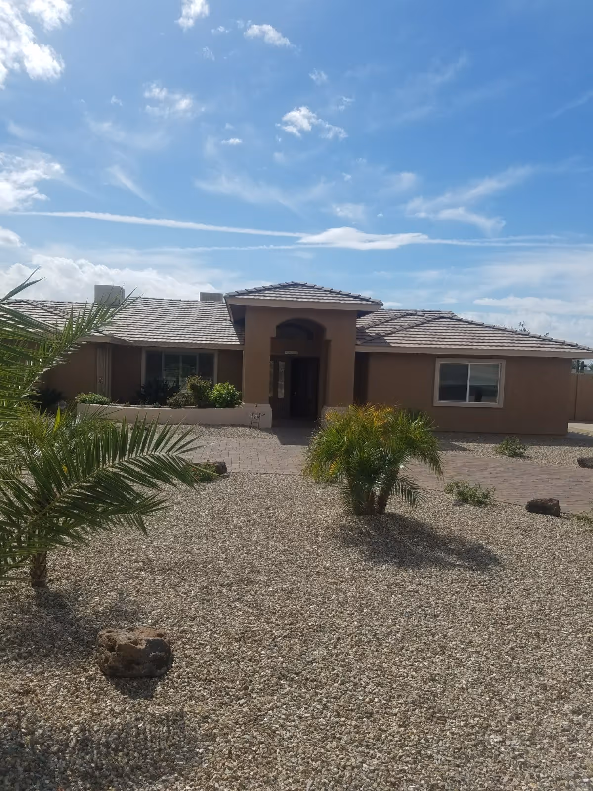 Single-story tan assisted living building with arched entrance and desert landscaping in front