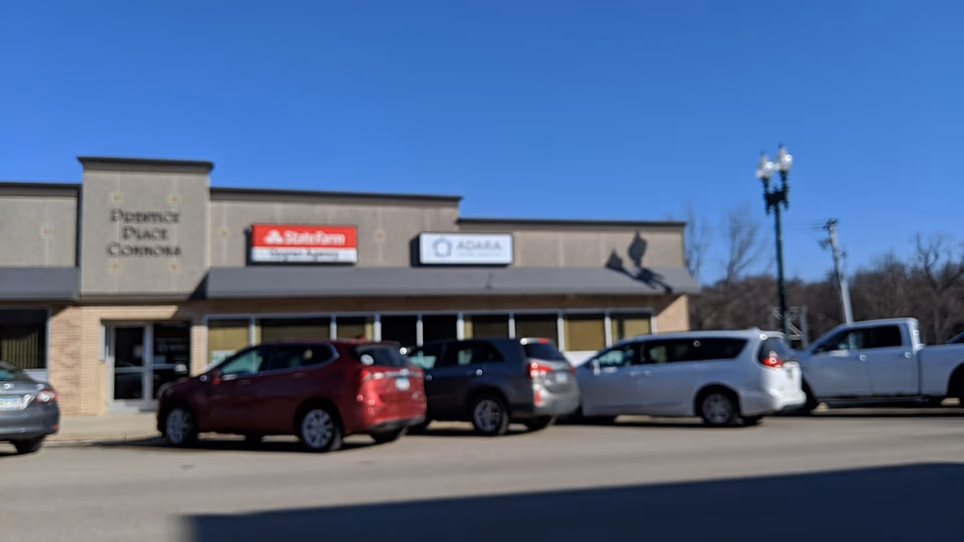 Exterior view of a strip mall storefront with Adara Home Health signage and parked cars.