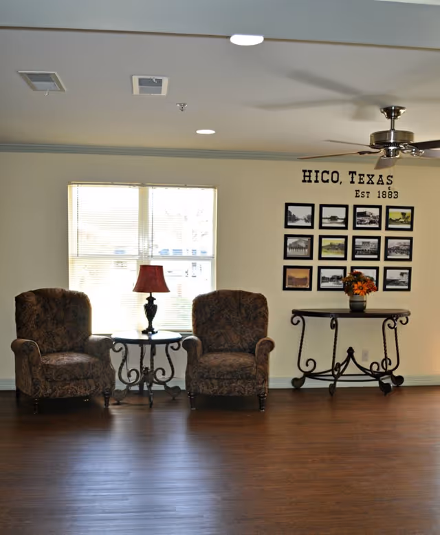 Interior living room with two upholstered chairs, a side table lamp, and wall photo collage.