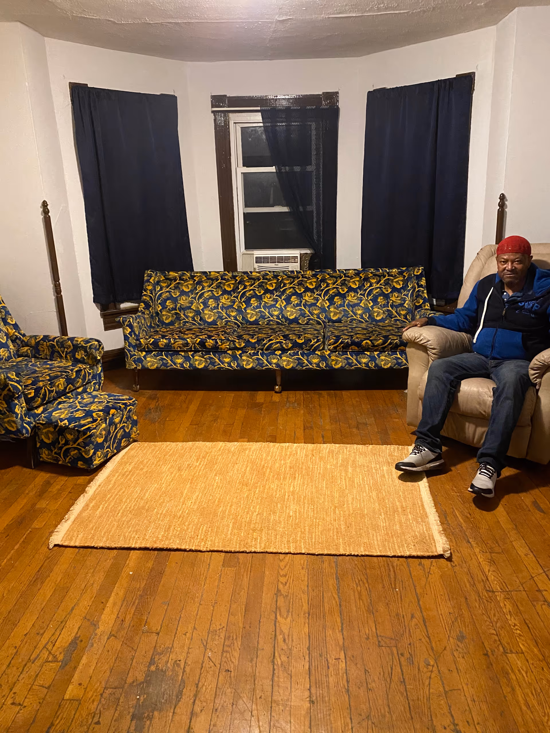 Cozy living room with patterned couches, wooden floor, and a man seated.