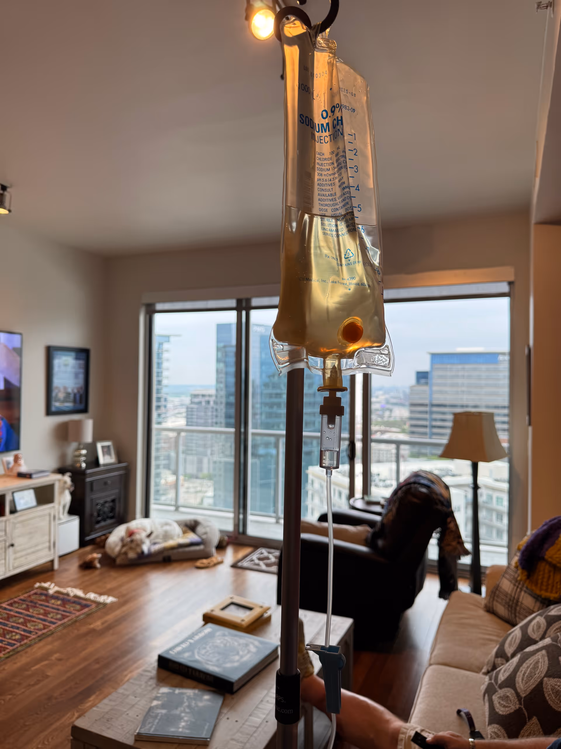 IV bag on stand in living room with couch, coffee table, and city view