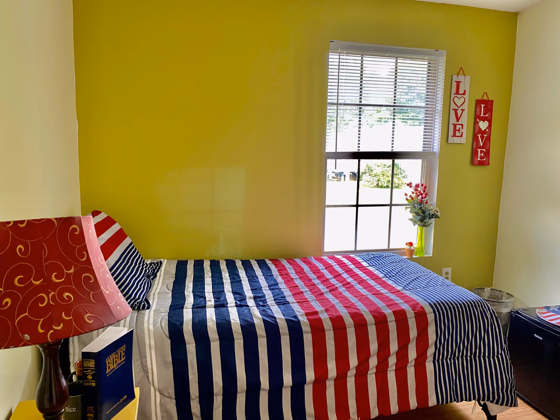 Bright bedroom with lime walls, red-white-blue striped bedspread, window, and LOVE decor.