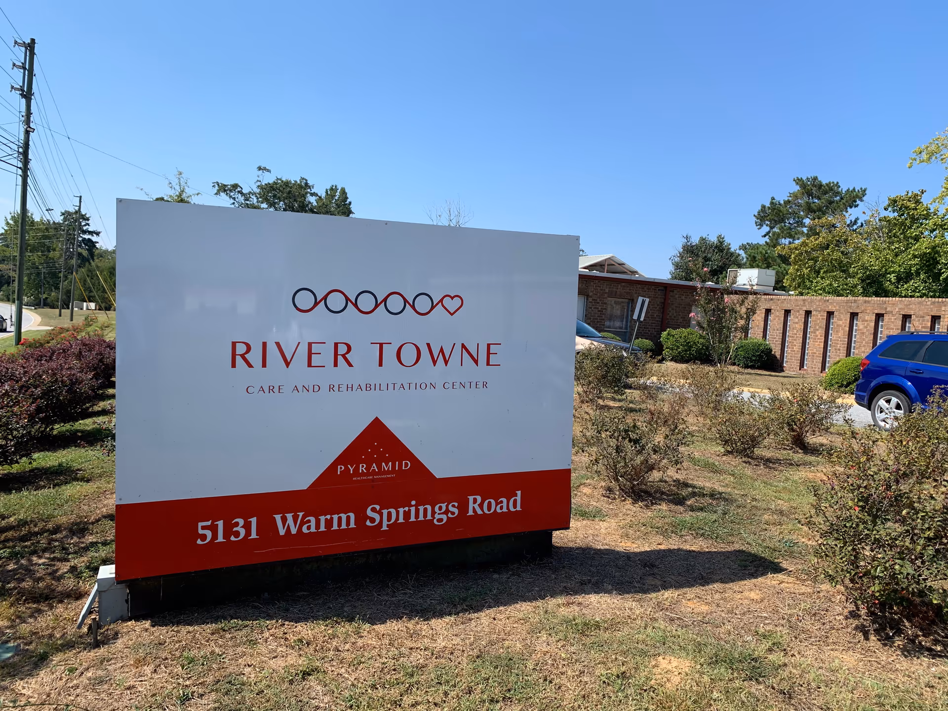 A large River Towne sign sits on a lawn with the building behind.