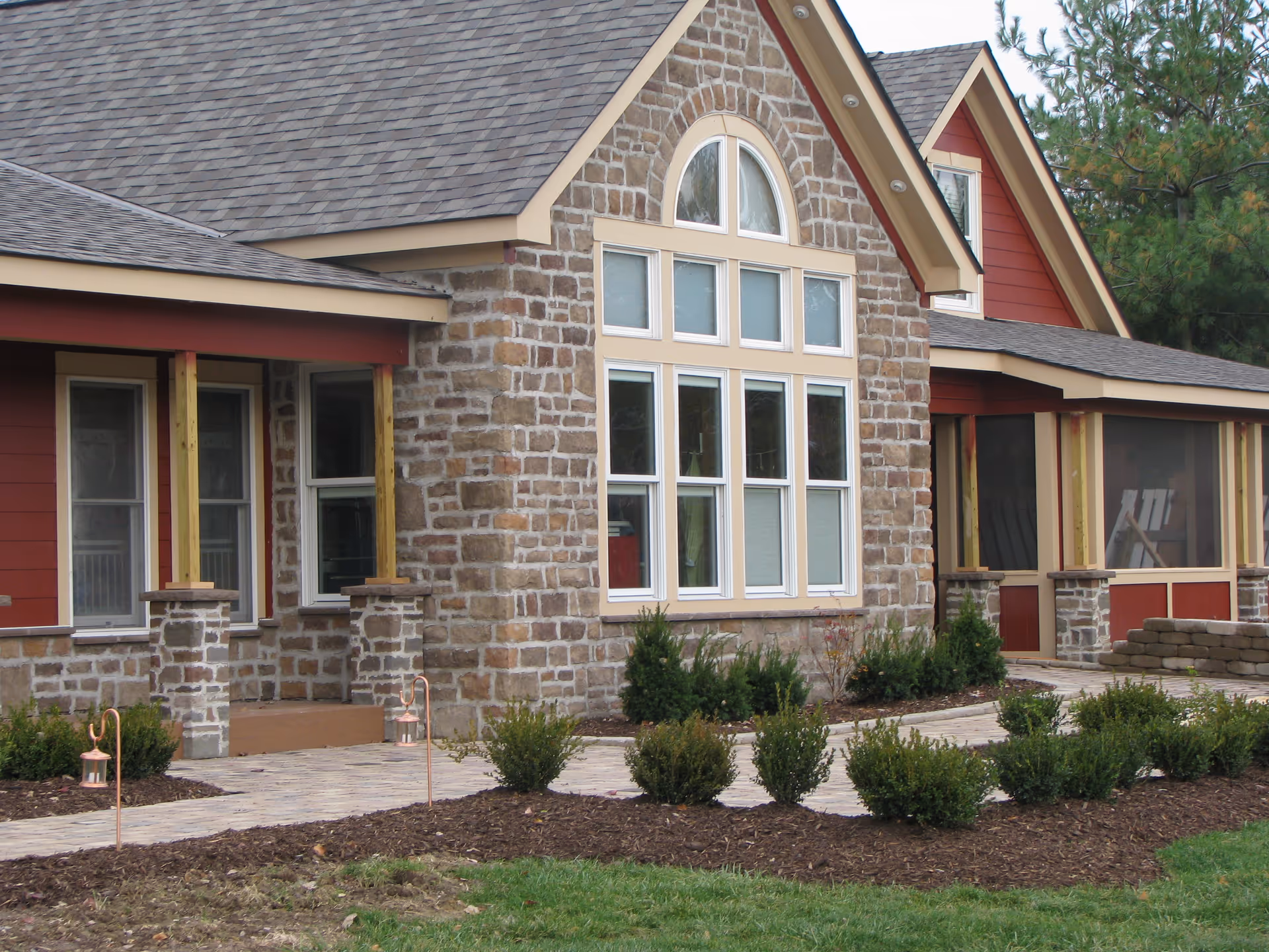 Stone and red siding senior living facility front with large arched windows and landscaping.
