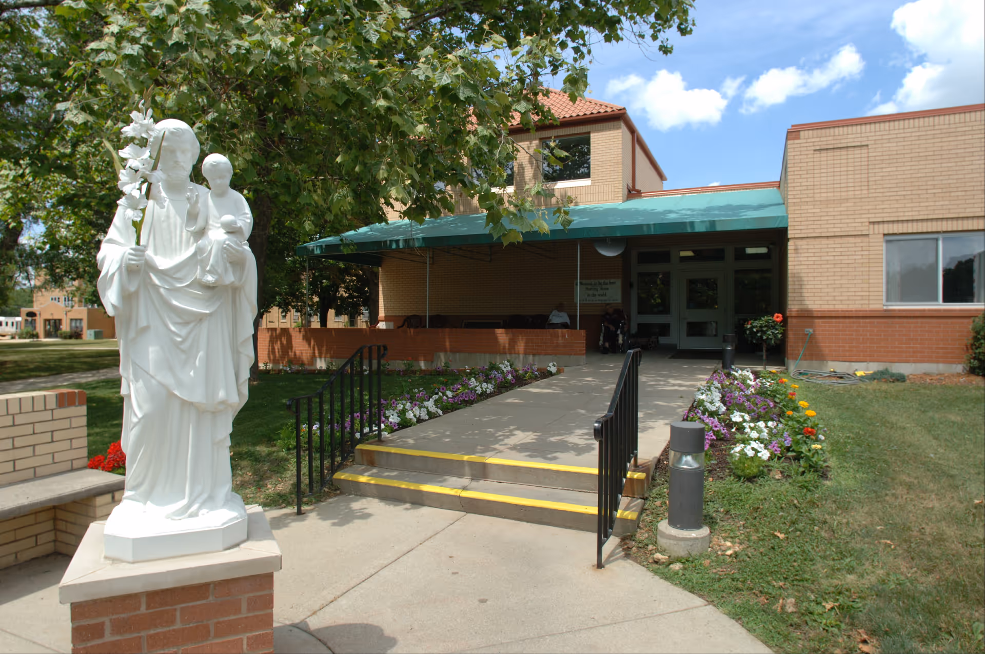 Exterior view of Ascension Saint Joseph Village entrance with statue and flowers.