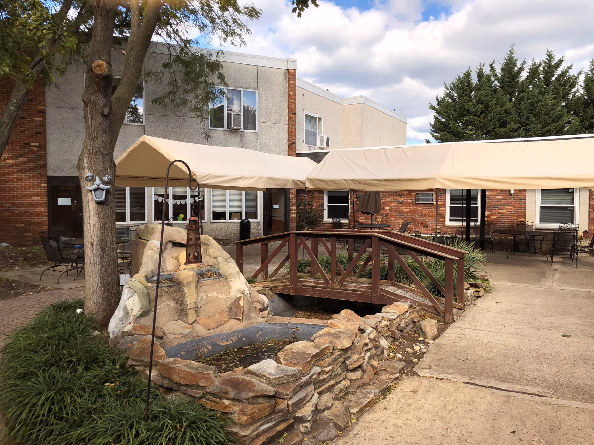 Outdoor courtyard at Laurel Bay Health & Rehabilitation Center with fountain, bridge, and beige canopies.