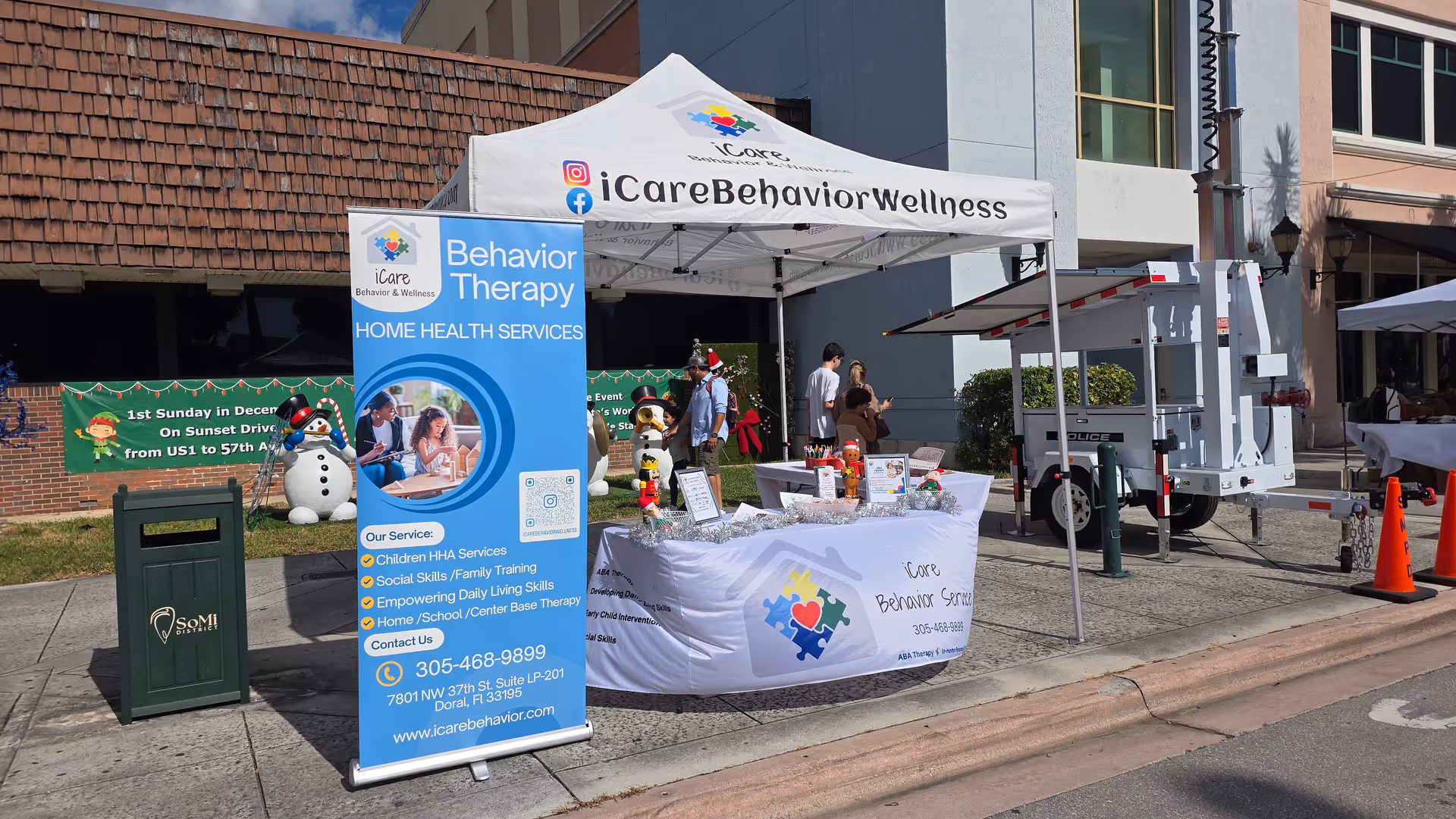 Outdoor iCare Behavior and Wellness booth with banners, tables, and attendees.