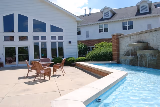 Outdoor pool area beside a white building with glass doors and patio seating.