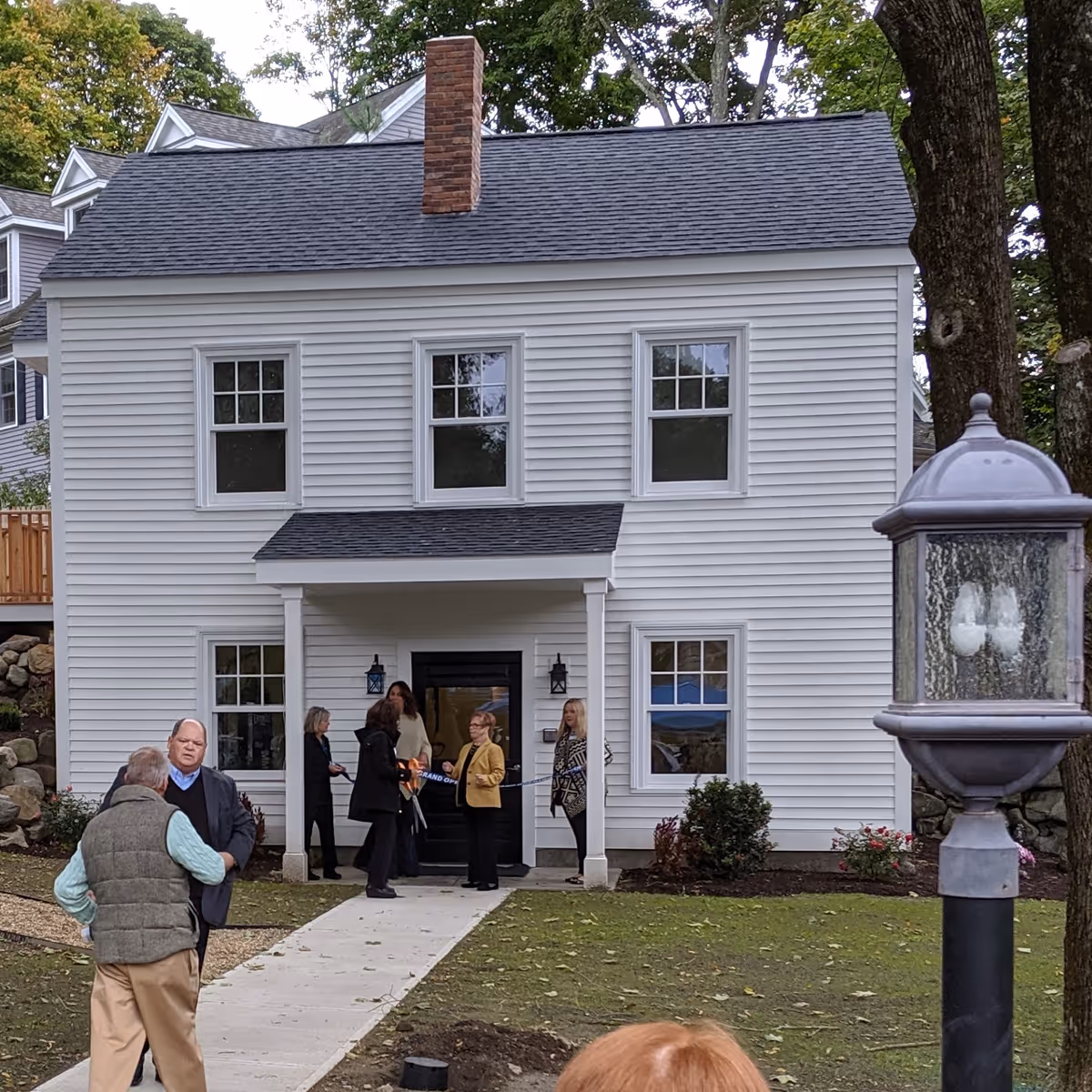 White two-story house with porch and people gathered near entrance.