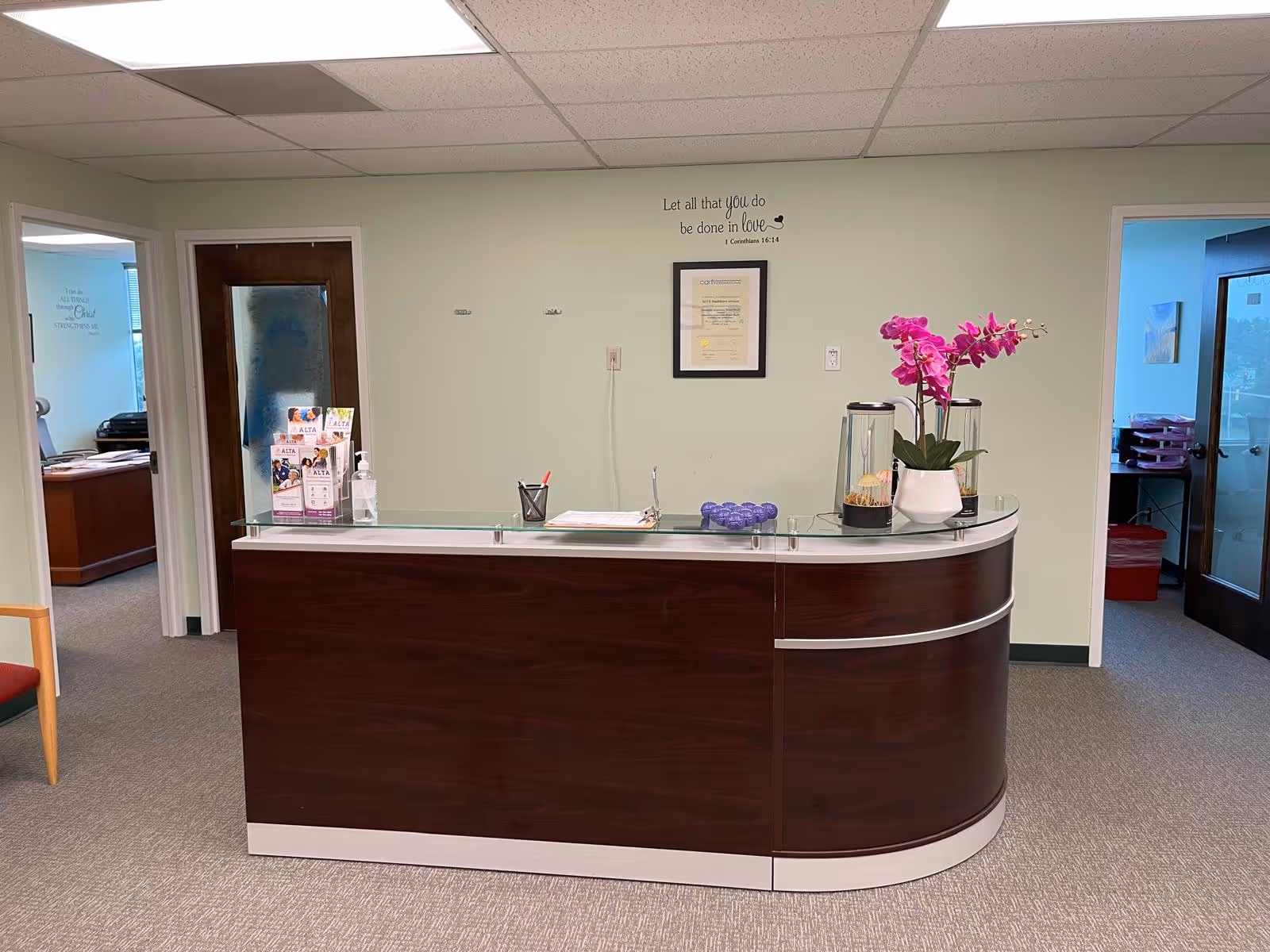 Reception desk in a pastel interior with framed certificate and orchid plant on glass top.