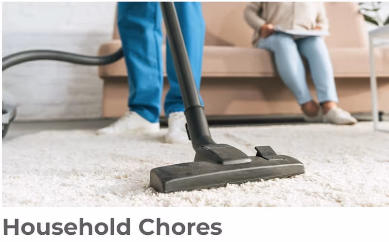 Vacuum cleaner on a carpet in a living room with a caregiver and resident nearby.