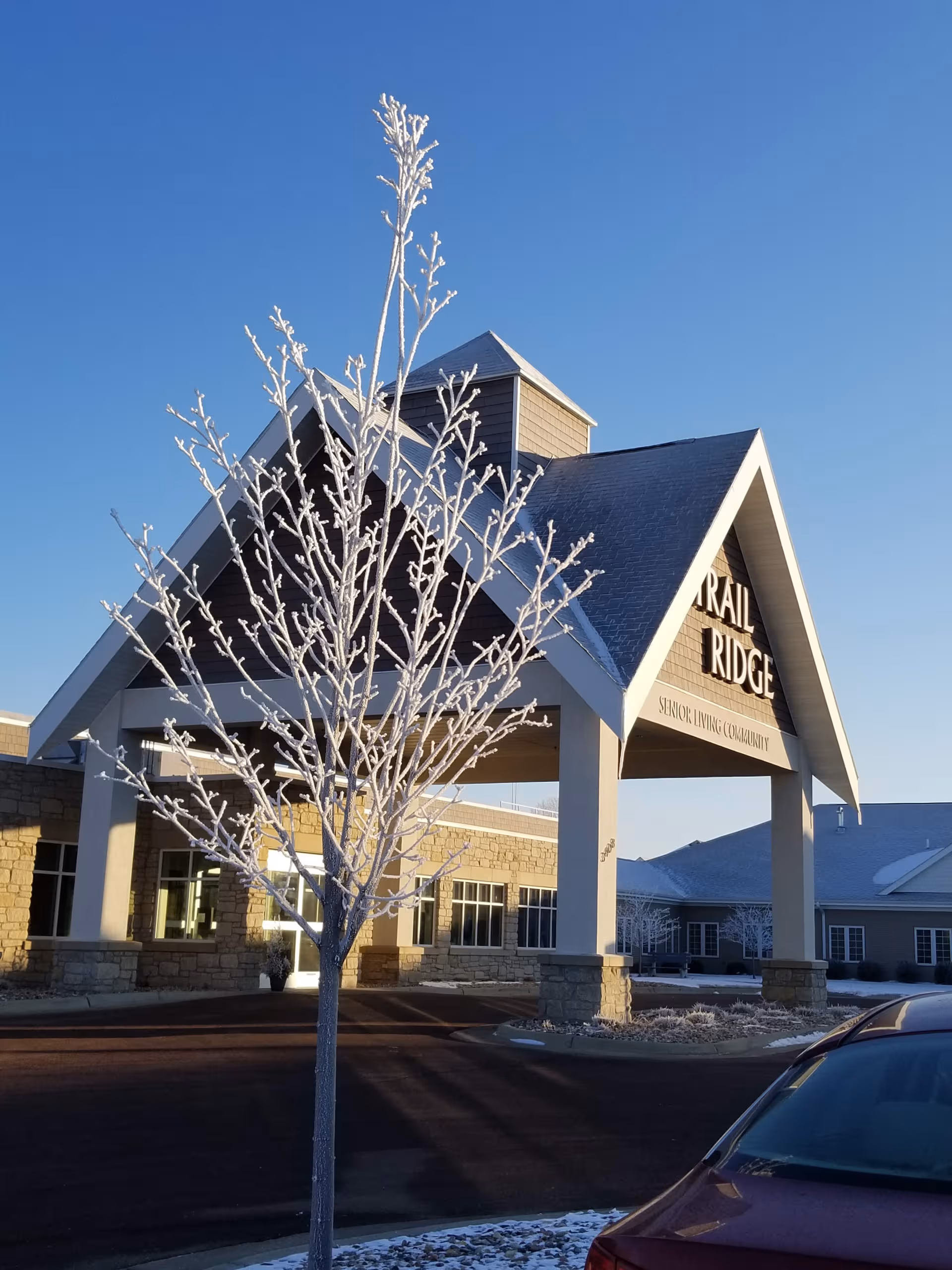 Exterior view of Trail Ridge Senior Living Community entrance with frosted tree