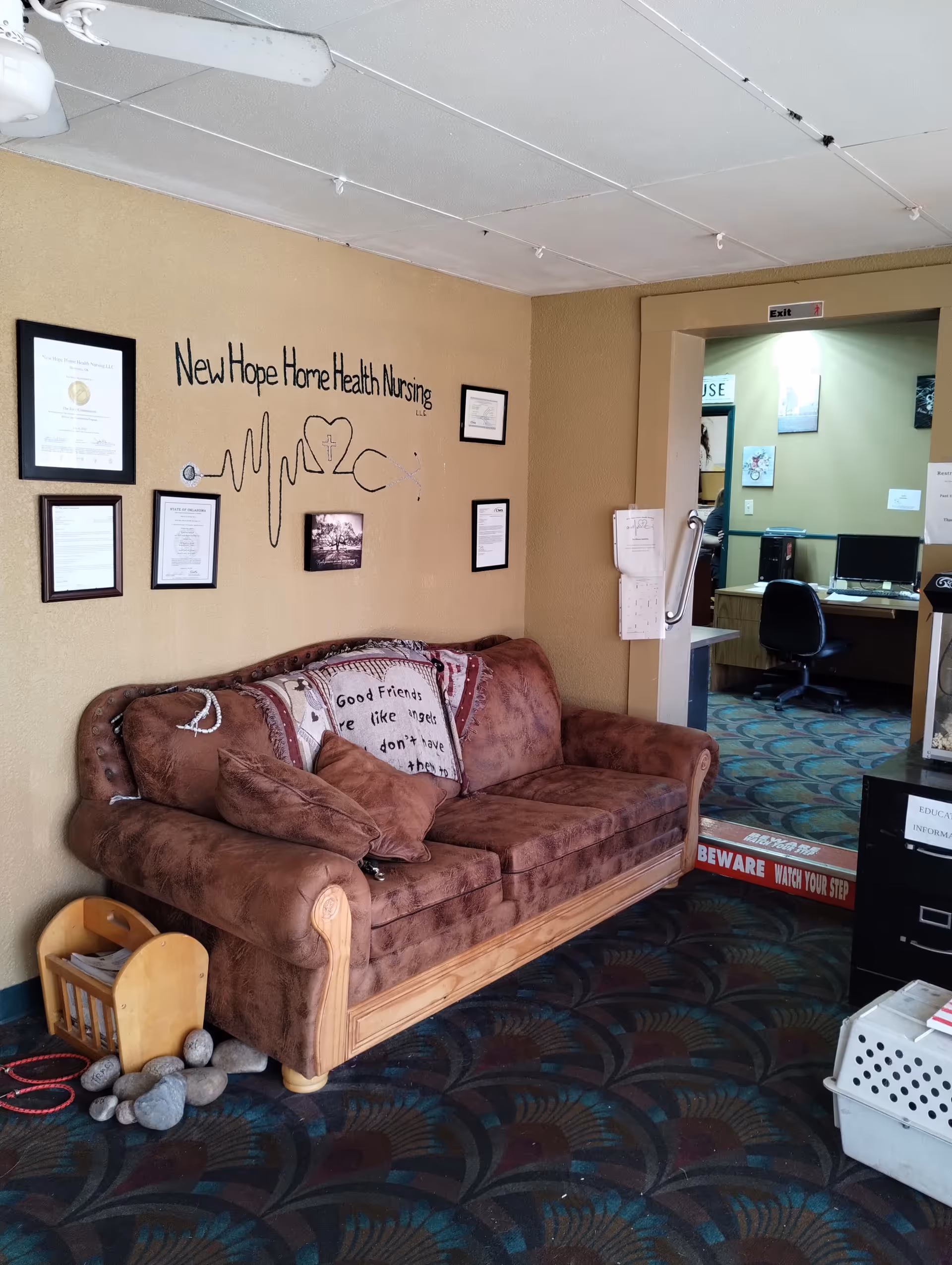 Cozy lounge area with a sofa, framed certificates, and an office doorway.