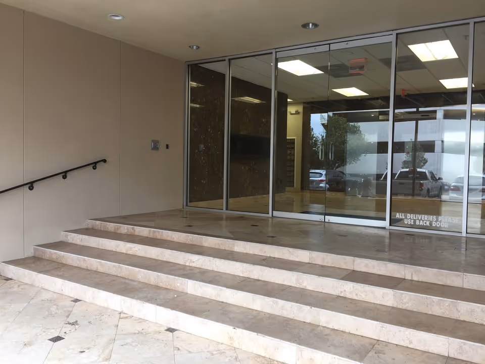 Wide marble steps lead to glass doors at a modern building entrance.
