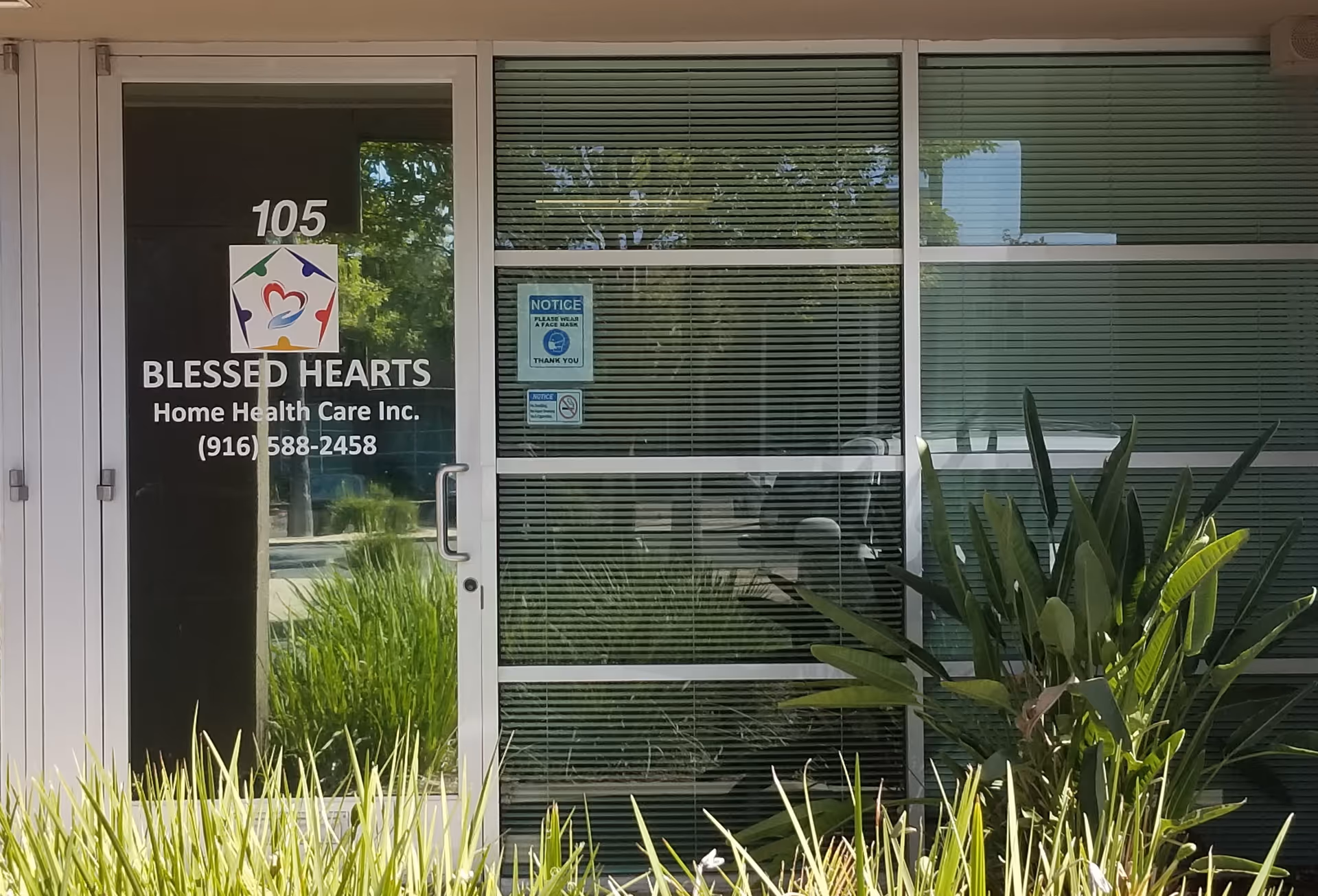 Entrance to Blessed Hearts Home Health Care building with glass doors and greenery.