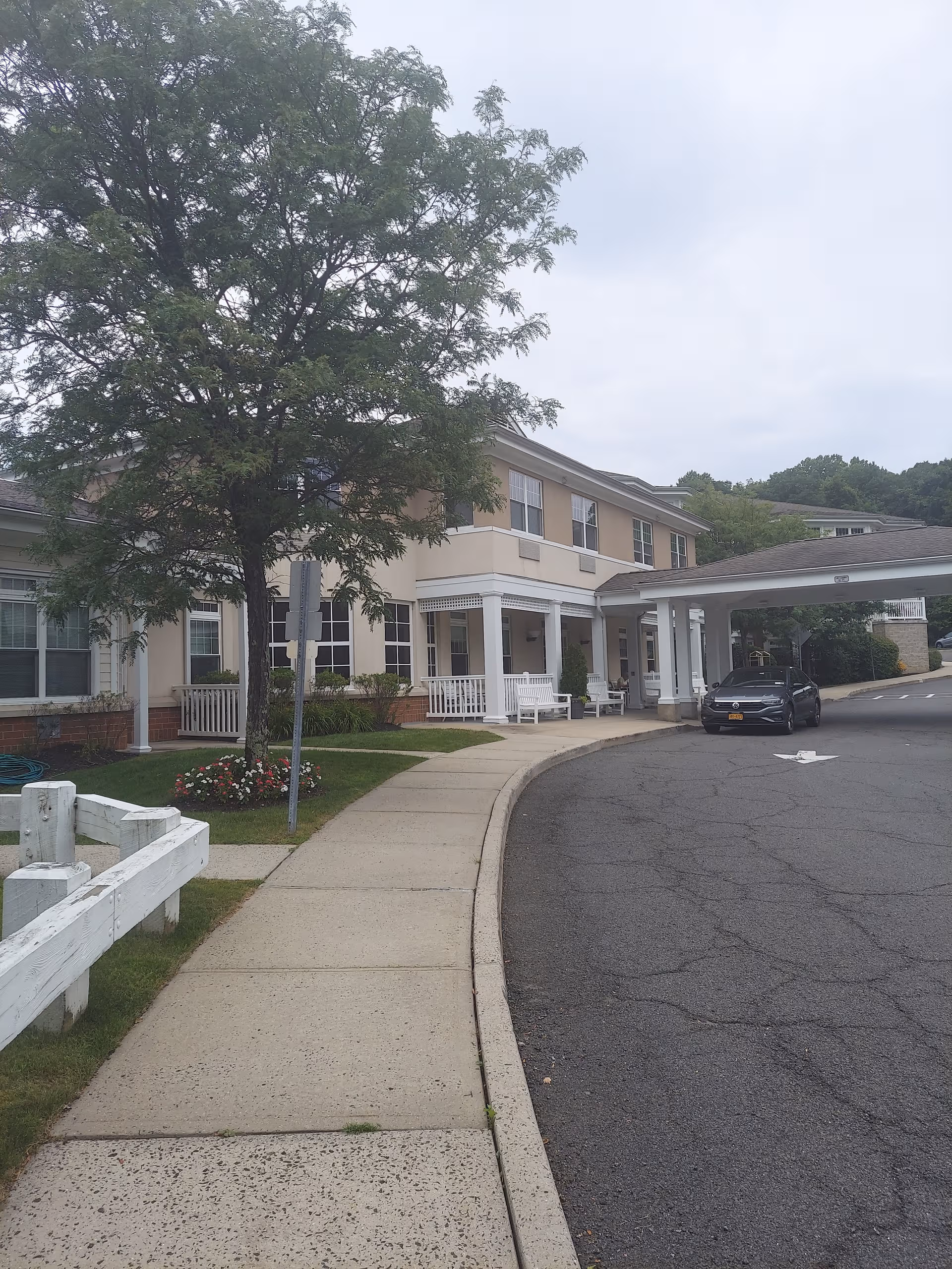 Exterior view of Atria Woodlands front entrance with sidewalk and parked car.