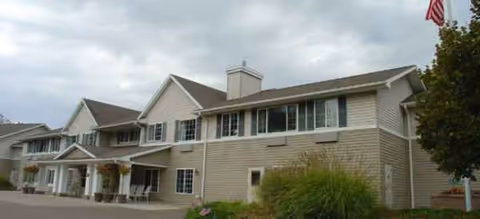 Senior living building with beige siding and a waving American flag on a cloudy day.