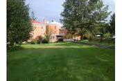 Sunny grassy lawn with trees and a brick senior living facility building in the background.