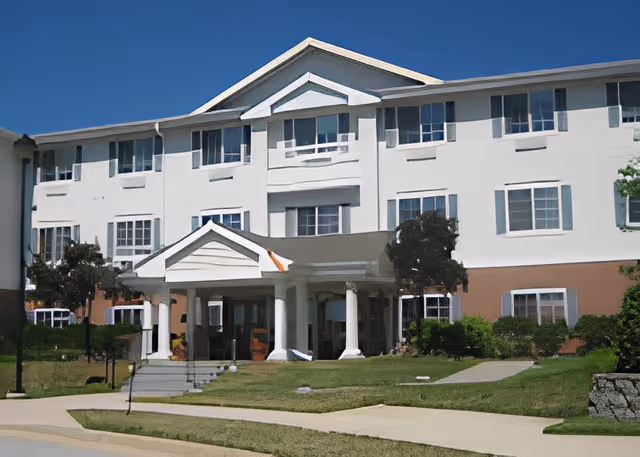 Front entrance of a three-story white senior living building with a covered portico and columns.