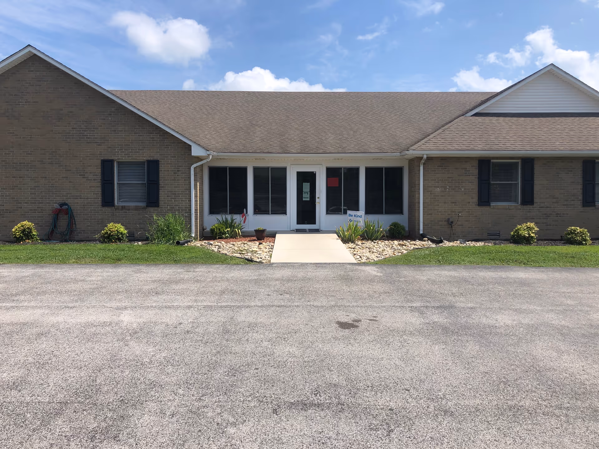 Brick single story senior living facility exterior with central glass entrance and landscaped front walkway.
