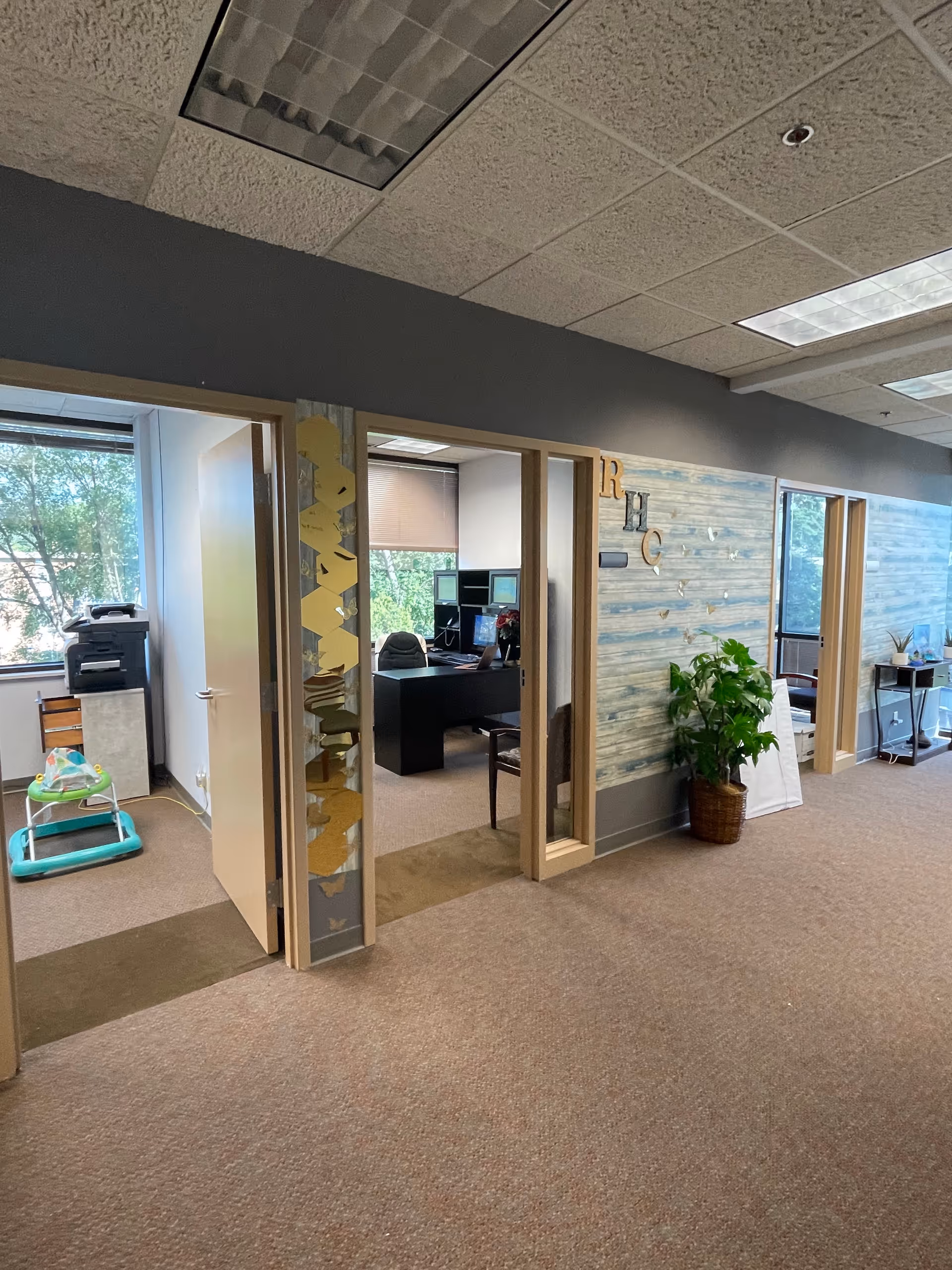 Interior hallway with office doors, desk, and potted plant in a senior care facility.