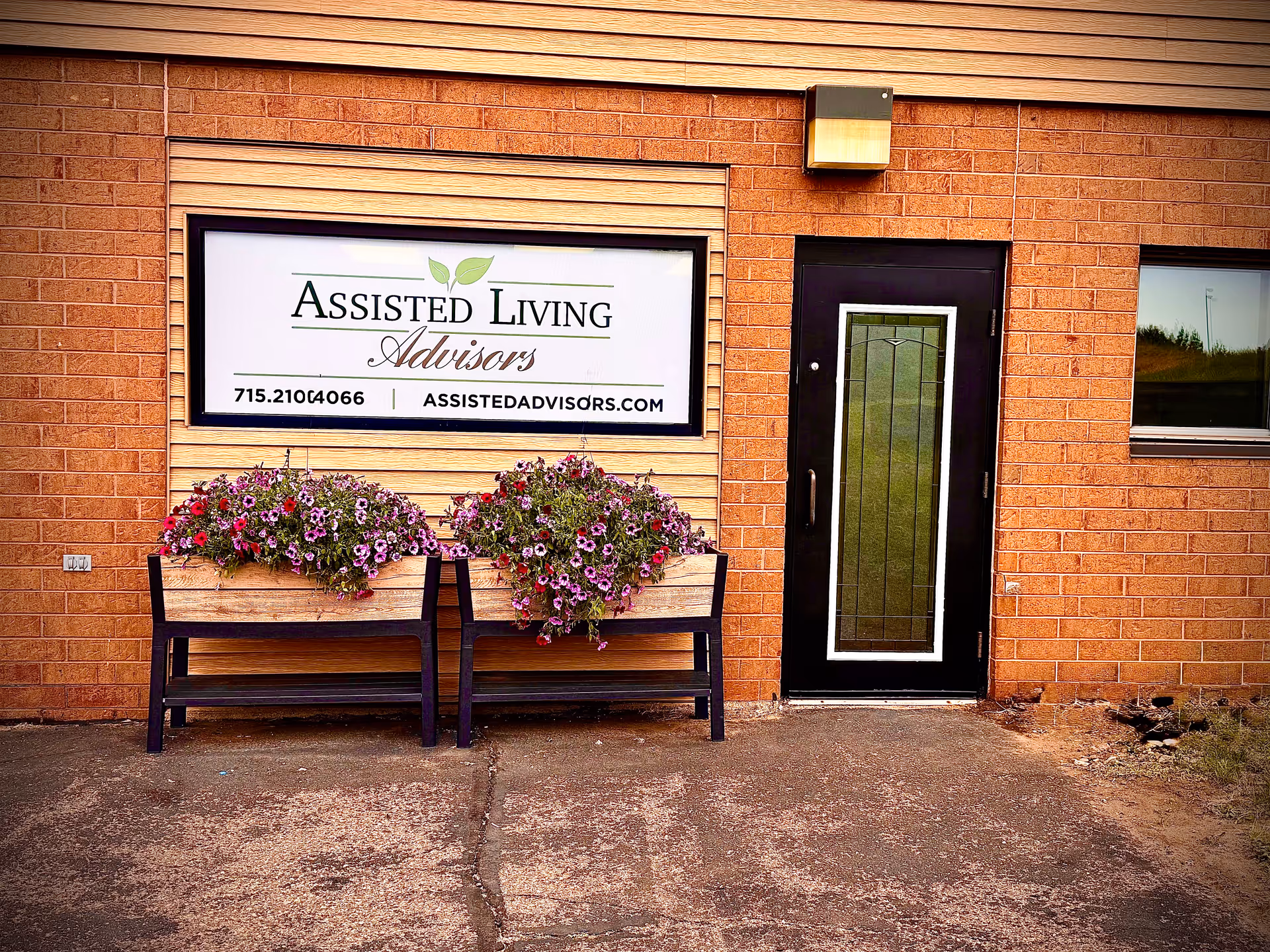 Brick exterior with a sign reading Assisted Living Advisors and two flower-filled benches.