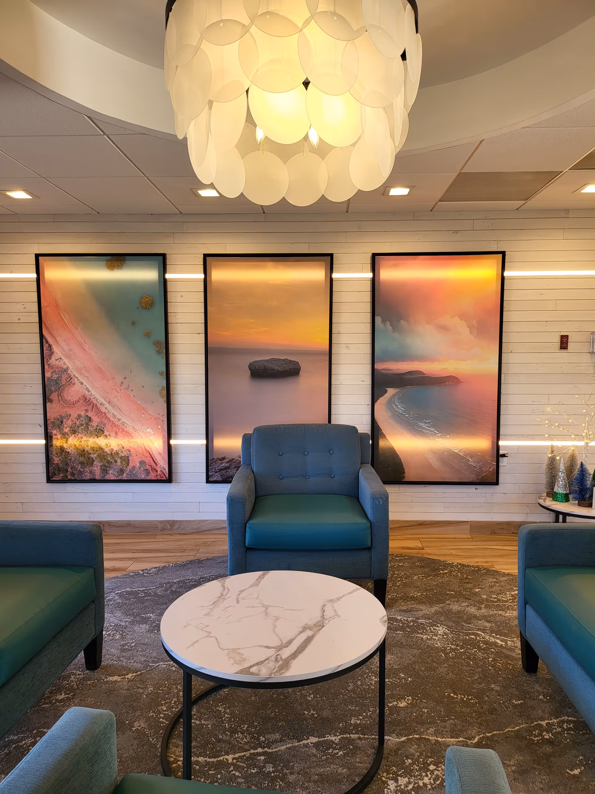 Contemporary interior lounge with blue chairs, a round marble table, and landscape art.