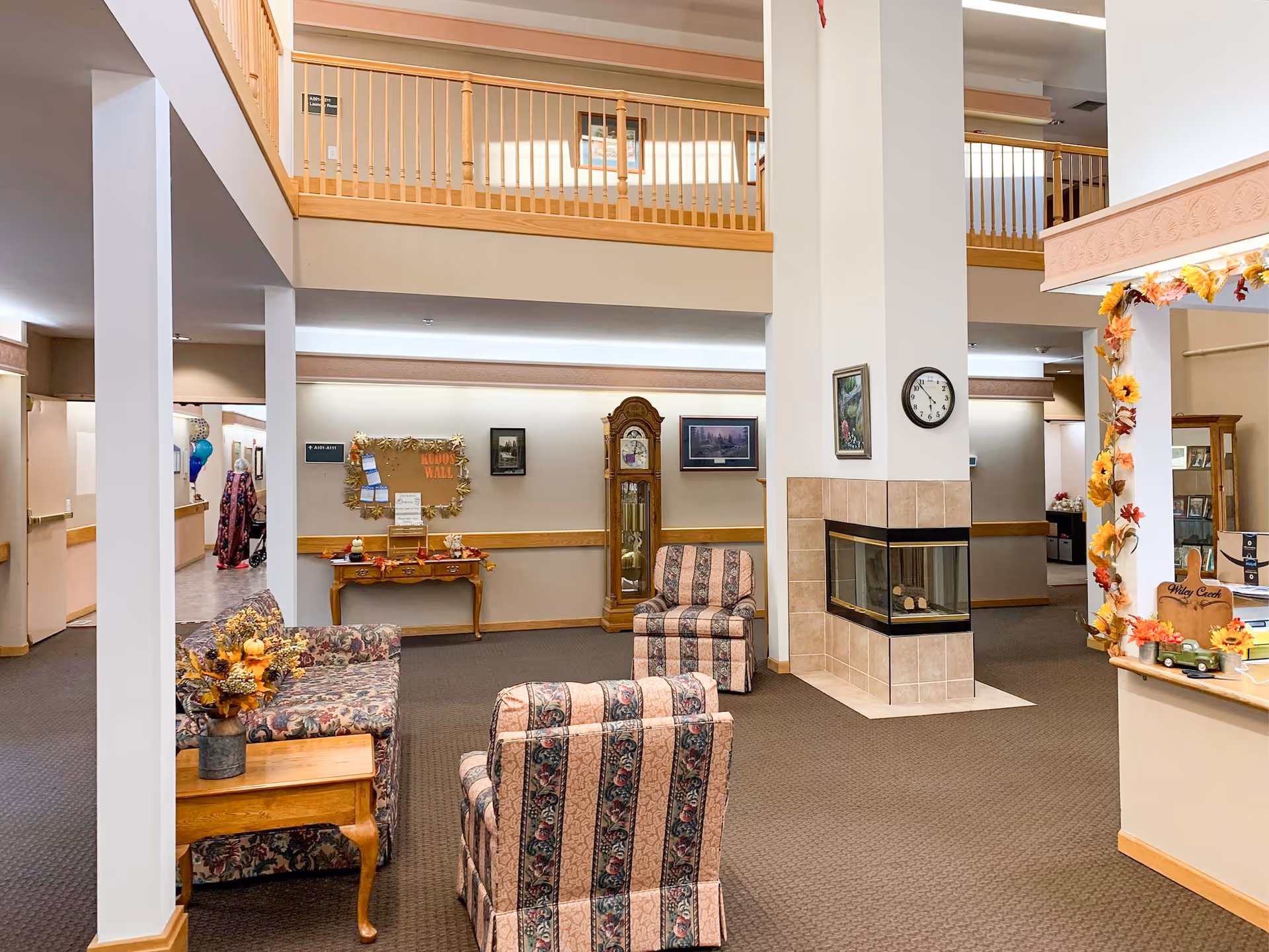 Bright lobby seating area in Wiley Creek Memory Care with fireplace and second-floor balcony.