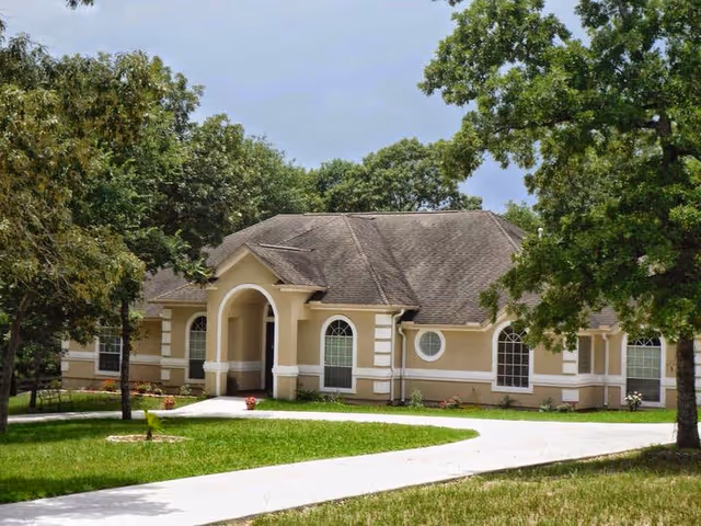 Front view of Angels Place Senior Living building with arched entrance, trees, and green lawn.